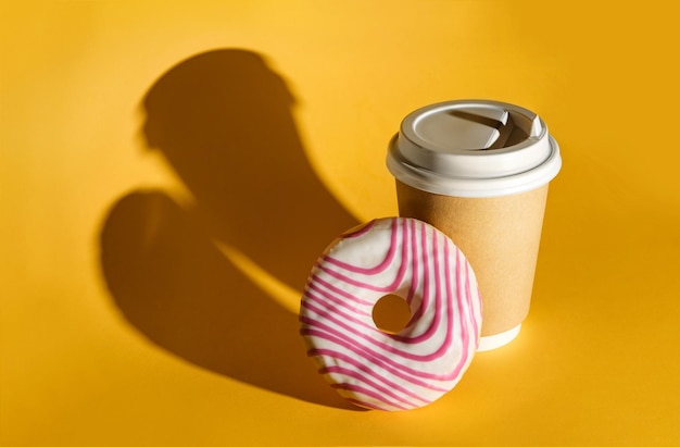 Un beignet et un verre de café éclairés par le soleil sur fond jaune,