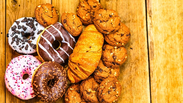 Des beignets colorés, des pâtisseries et des biscuits sur une table en bois, du sucre glacé sucré, des beignets avec du glaçage au chocolat, une vue supérieure avec un espace de copie.