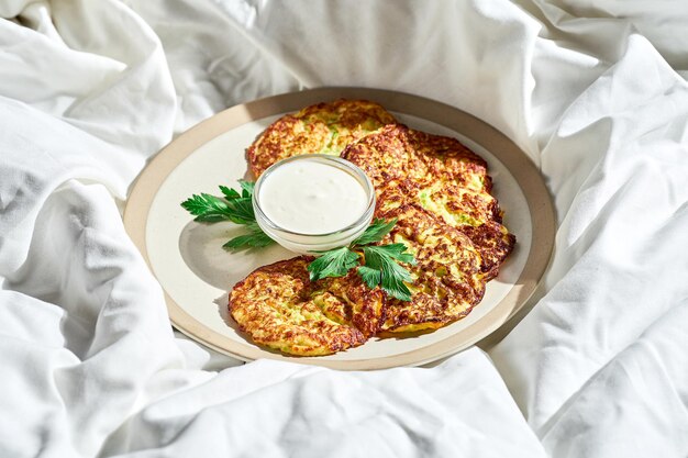 Beignets de courgettes à la crème sure dans une assiette sur une feuille blanche Lumière dure