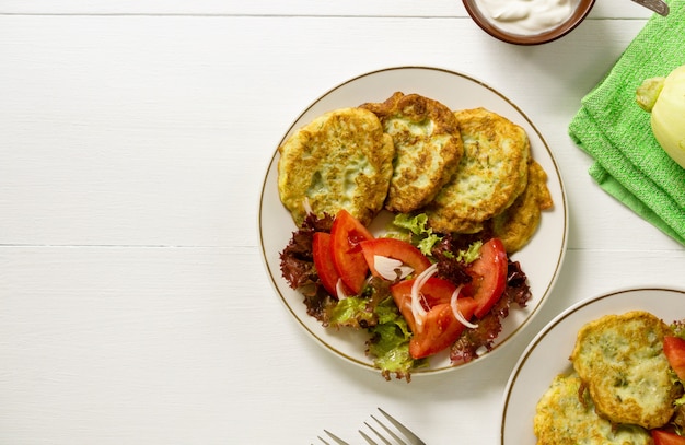 Beignets de courgettes avec salade de tomates sur un tableau blanc.