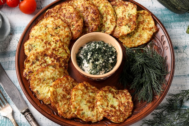 Les beignets de courgettes sont disposés sur une assiette, au centre il y a une sauce à la crème sure à l'ail et à l'aneth