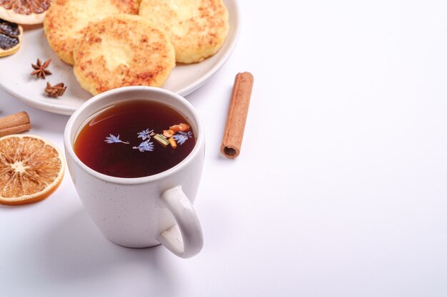 Photo beignets de fromage cottage avec thé aromatique noir chaud, ambiance de petit-déjeuner de noël à l'anis et à la cannelle sur fond blanc, espace de copie de vue en angle