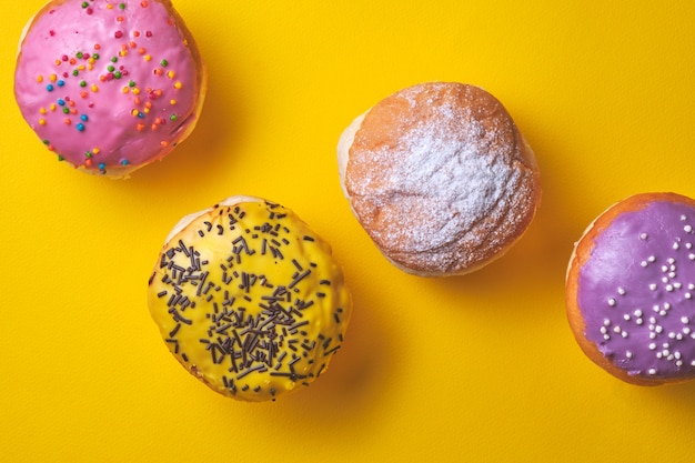 Beignets avec glaçage coloré sur fond de papier jaune.