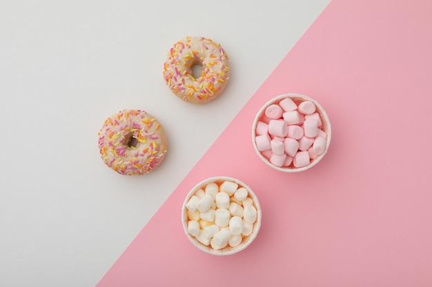 Des beignets et des marshmallows dans des tasses en papier sur fond rose et blanc