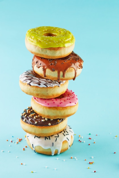 Beignets multicolores avec glaçage et saupoudrage empilés dans une pile sur un fond bleu.