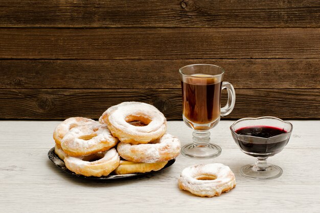 Beignets en sucre en poudre, une tasse de thé et de confiture de groseilles sur un fond en bois