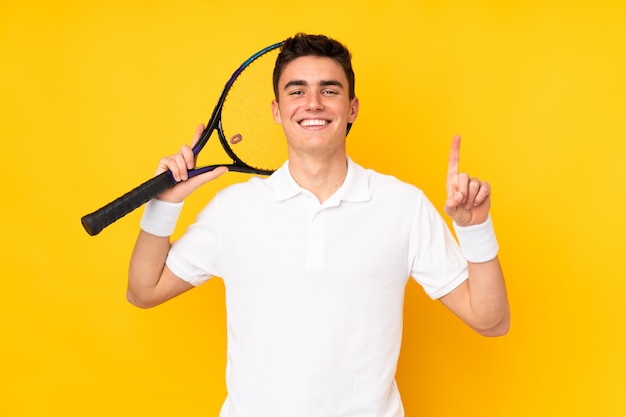 Bel adolescent joueur de tennis homme sur mur jaune jouant au tennis et pointant vers le haut