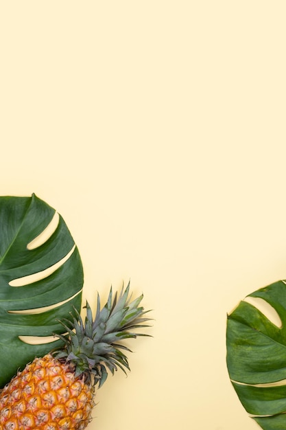 Bel ananas sur feuilles de palmier tropical monstera isolé sur fond jaune pastel clair vue de dessus plat posé au-dessus des fruits d'été