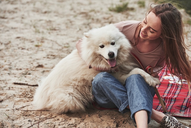 Bel animal. Une fille blonde avec son mignon chien blanc passe un bon moment sur une plage.