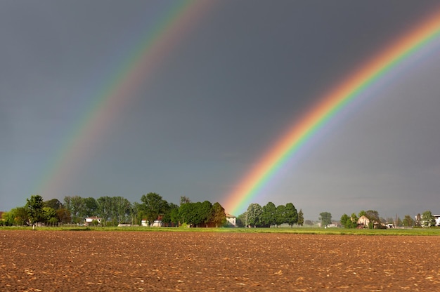 Un bel arc-en-ciel coloré double dans le contexte d'un ciel orageux dangereux au-dessus d'une ferme rurale