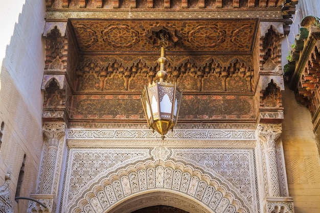 Bel art marocain. Plafond sculpté en bois, lampe antique et art arabesque au mur.