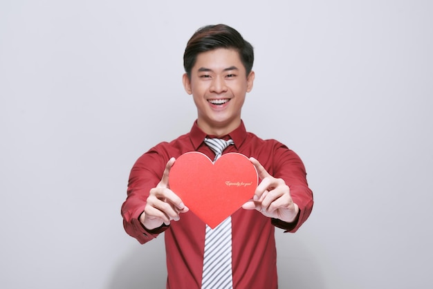 Un bel asiatique mignon tient un coeur rouge en papier pour la Saint-Valentin sur fond blanc avec espace de copie