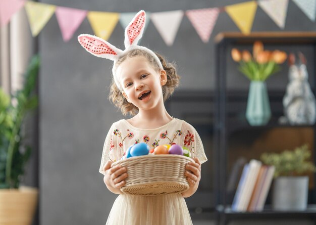 Bel enfant avec des oeufs de peinture Jolie petite fille porte des oreilles de lapin