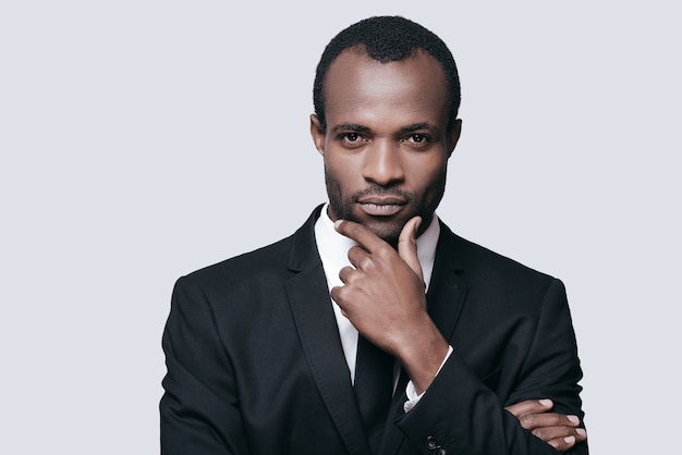 Photo bel entrepreneur. portrait d'un jeune homme africain confiant tenant la main sur le menton et regardant la caméra en se tenant debout sur fond gris