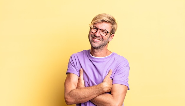 Bel homme adulte blond riant joyeusement avec les bras croisés, avec une pose détendue, positive et satisfaite