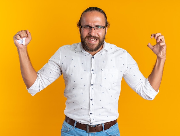 Bel homme adulte en colère portant des lunettes gardant la main dans l'air écrasant le papier à la main