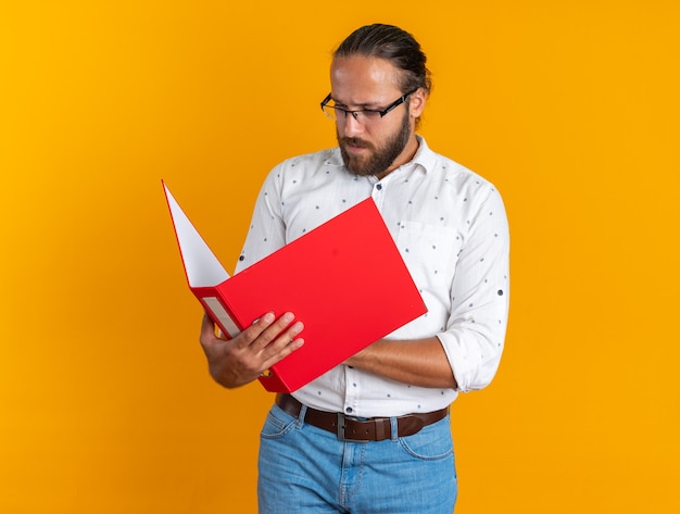 Bel homme adulte concentré portant des lunettes tenant et regardant le dossier ouvert