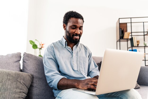 Bel homme adulte noir travaillant avec un ordinateur portable à la maison