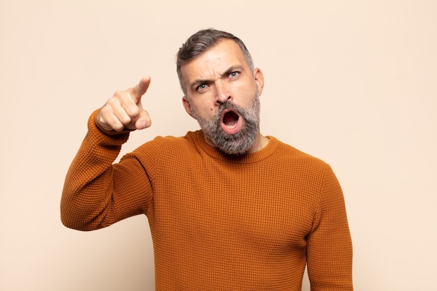 Bel homme adulte pointant vers la caméra avec une expression agressive en colère ressemblant à un patron furieux et fou