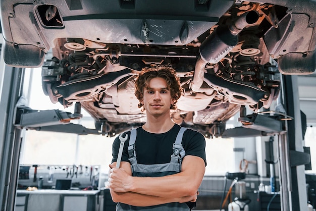 Bel homme adulte en uniforme de couleur grise debout sous l'automobile