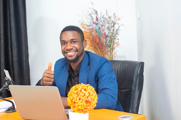 Bel homme d'affaires afro-américain en costume classique utilise un ordinateur portable et souriant tout en travaillant au bureau