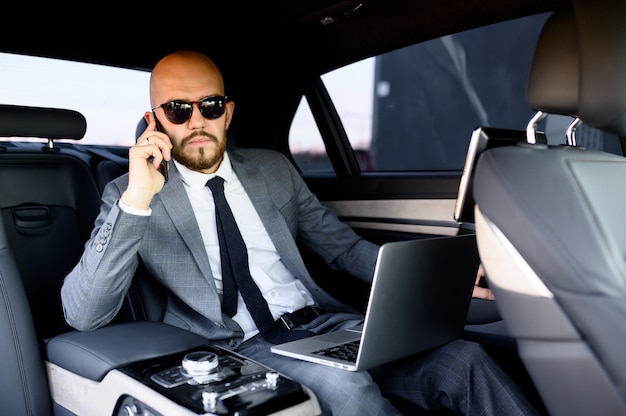 Bel homme d'affaires à l'aide de son téléphone portable dans une voiture moderne avec chauffeur au centre de la ville. Concept d'entreprise