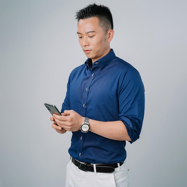 Bel homme d'affaires asiatique chemise vérifiant le mur gris isolé du téléphone