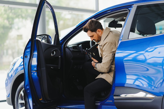 Bel homme d'affaires barbu est assis dans une nouvelle voiture chez un concessionnaire automobile