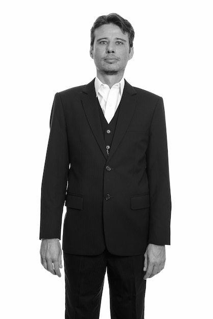 Bel homme d'affaires avec chaume de barbe en costume isolé contre un mur blanc en noir et blanc