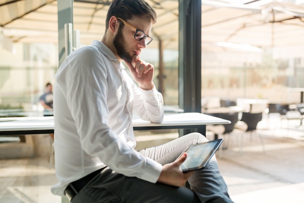 Bel homme d'affaires en chemise portant des lunettes à l'aide de tablet pc