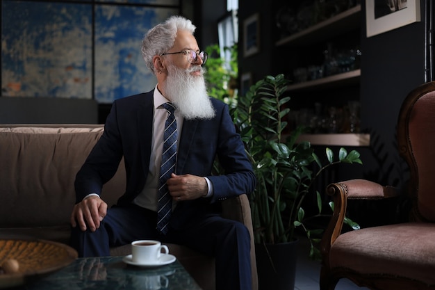 Un bel homme d'affaires confiant et réfléchi pensant tout en étant assis sur un canapé dans son bureau moderne sur le concept d'entreprise. Pause café.