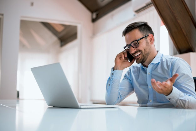 Bel homme d&#39;affaires à lunettes utilise un ordinateur, parler au téléphone mobile.