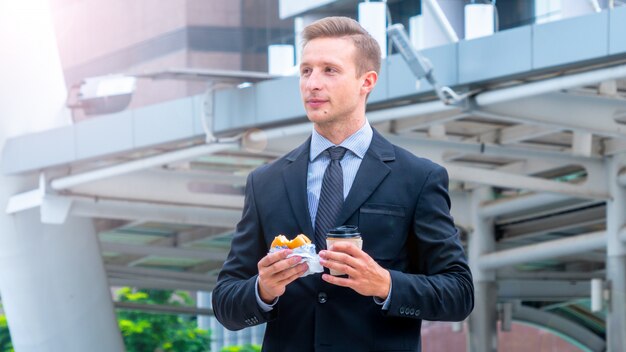 Bel homme d'affaires, manger le petit déjeuner hamburger de restauration rapide et boire une tasse de café