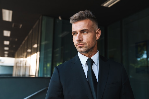 un bel homme d'affaires mature aux cheveux gris à l'extérieur dans la rue près du centre d'affaires.