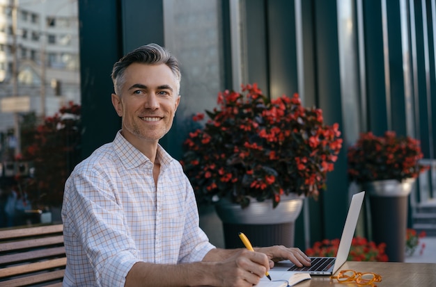 Bel homme d'affaires mature utilisant un ordinateur portable, prendre des notes, planifier le démarrage