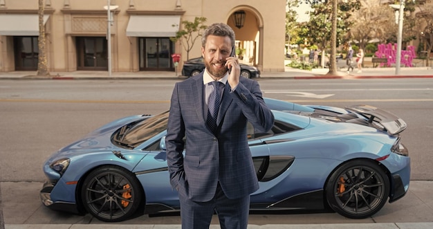 Bel homme d'affaires parle au téléphone à côté d'une voiture de luxe