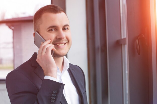 Bel homme d'affaires portant un costume noir à l'aide du téléphone