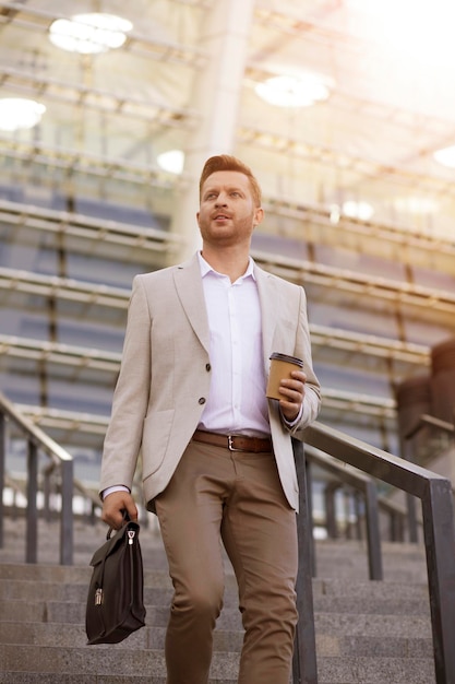 Bel homme d'affaires regardant loin et gardant le café à la main tout en descendant les escaliers