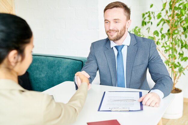 Bel homme d'affaires se serrant la main avec un partenaire à la table de réunion