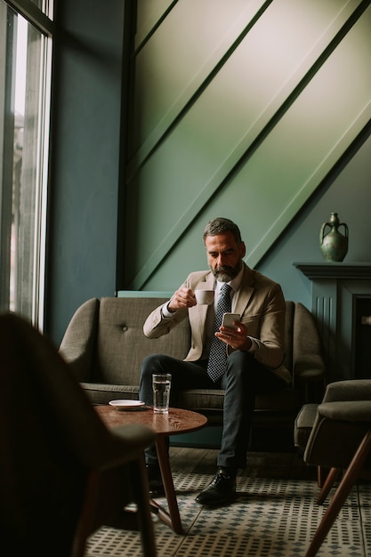 Bel homme d&#39;affaires senior, boire du café et à l&#39;aide de téléphone portable dans le hall