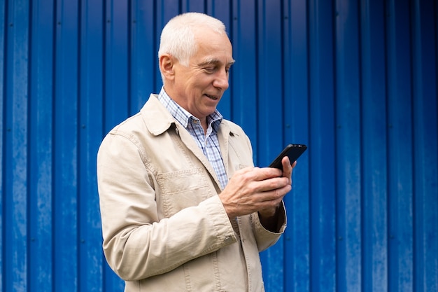 Bel homme d'affaires senior en tenue décontractée, debout à l'extérieur avec smartphone