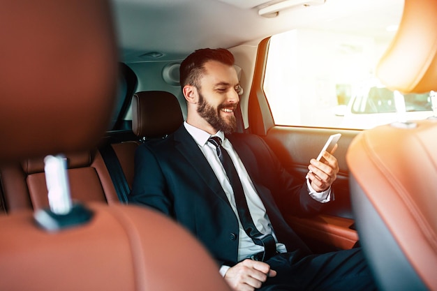 Bel homme d'affaires avec téléphone à portée de main assis sur la banquette arrière du gars de la voiture en détournant les yeux