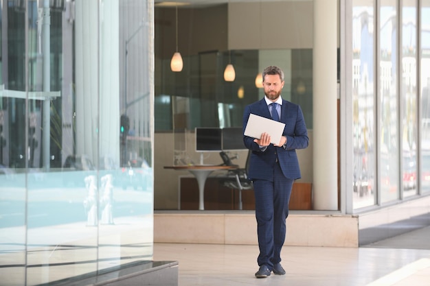 Bel homme d'affaires tenant son ordinateur portable debout dans la rue