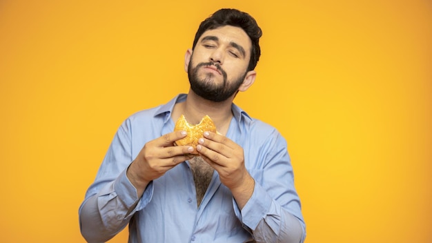 Un bel homme affamé tient un hamburger à la main sur fond jaune