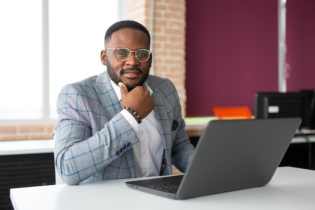 Bel homme africain adulte à table avec ordinateur portable au travail