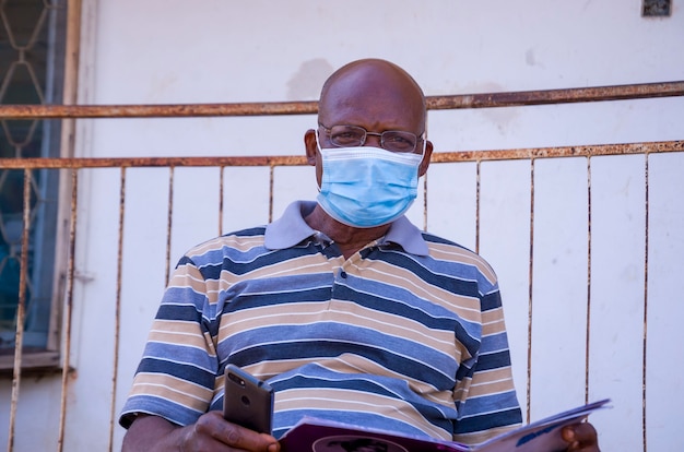 Bel homme africain âgé portant un masque facial se sentant excité alors qu'il lit le livre sur ses genoux.