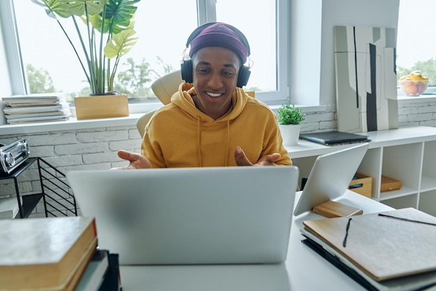 Un bel homme africain avec des écouteurs fait un appel vidéo alors qu'il travaille au bureau.