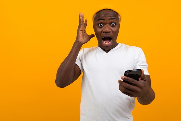 Bel homme africain noir regarde avec surprise au téléphone sur un jaune