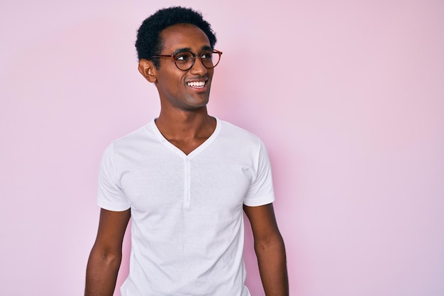 Bel homme africain portant des vêtements décontractés et des lunettes regardant de côté avec le sourire sur le visage, expression naturelle. rire confiant.