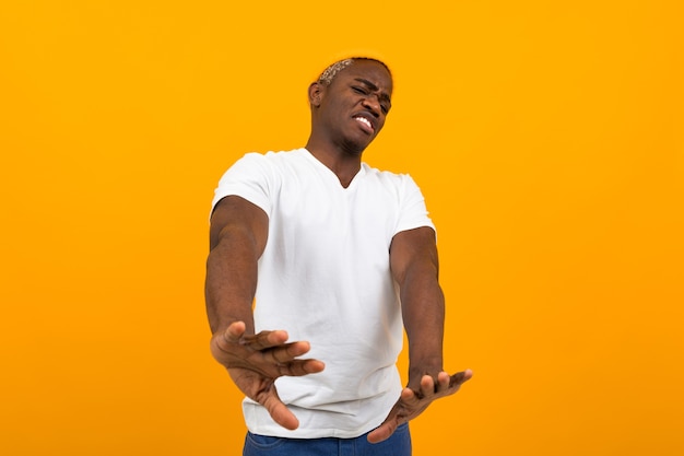 Bel homme africain souriant dans un t-shirt blanc agitant ses mains dans le déni sur un fond orange.